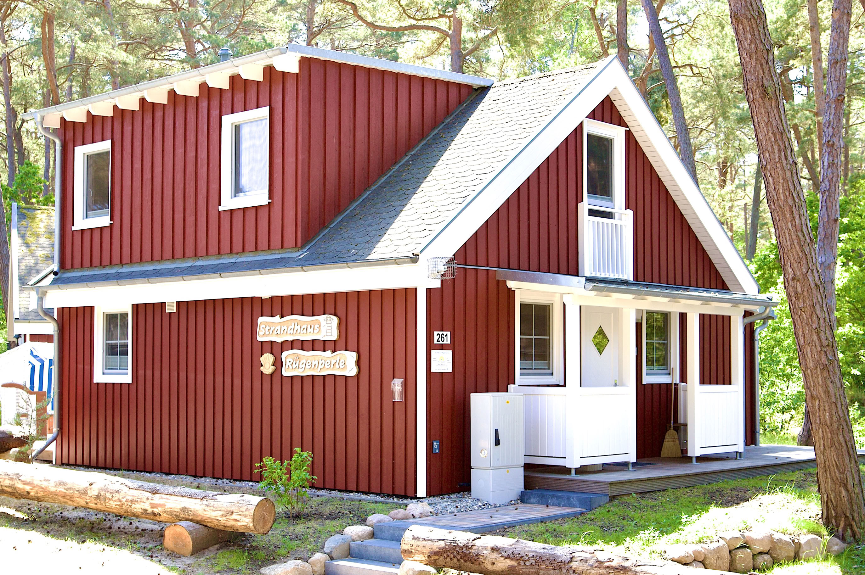 Rotes Holz-Ferienhaus mit weißem Dach und Veranda, umgeben von Bäumen.