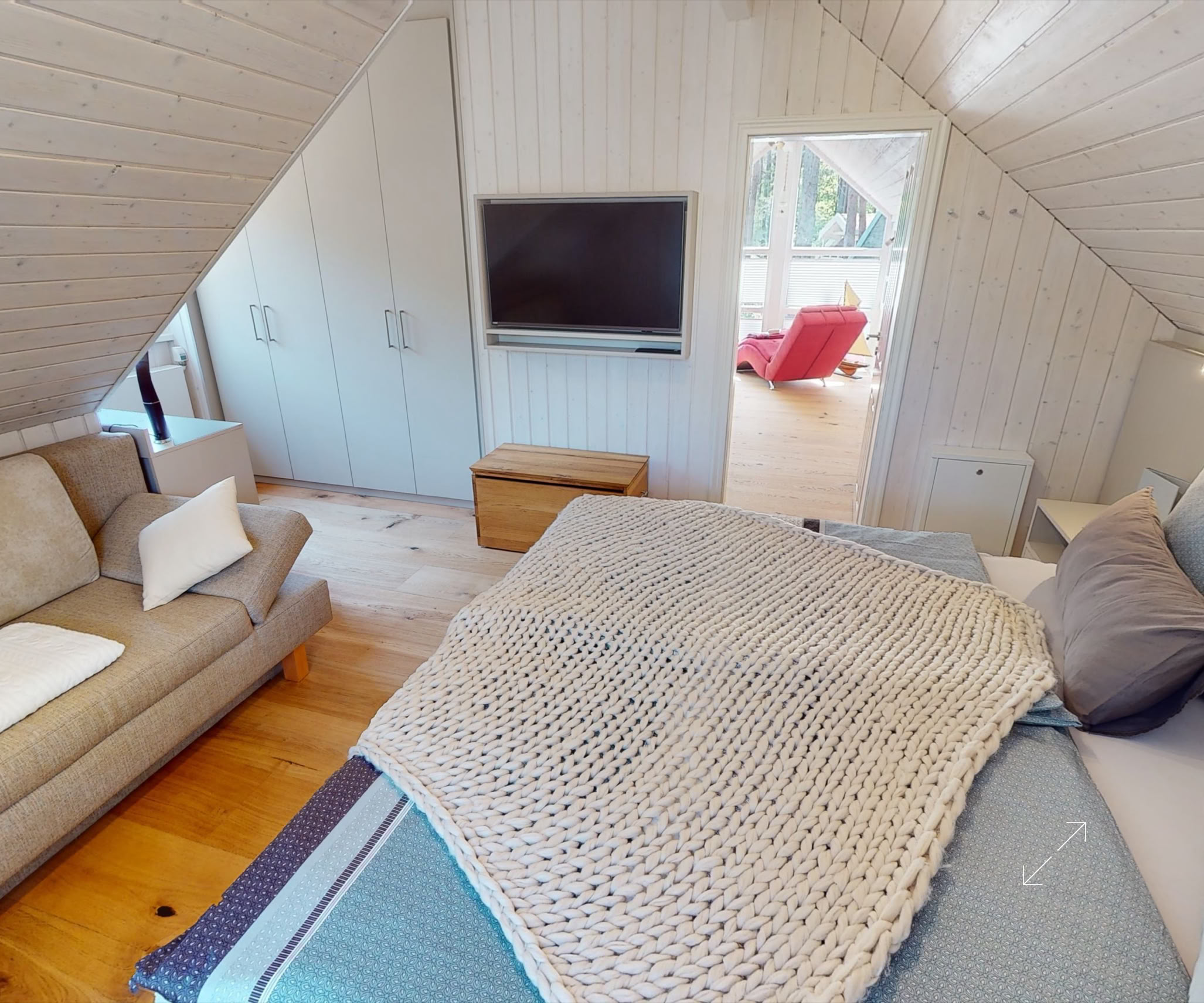 Dachzimmer mit einem Bett, einem Sofa, einem Fernseher an der Wand und einem kleinen Holztisch.