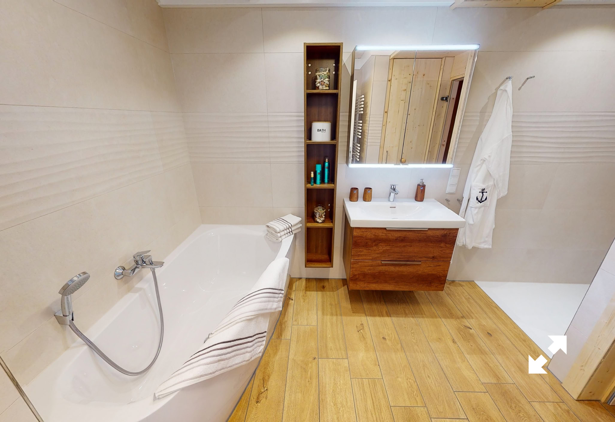 Modernes Badezimmer mit Badewanne links, Waschbecken und Spiegel in der Mitte, Holzregal daneben und Handtuch an der Wand rechts. Holzboden und helle Wände.