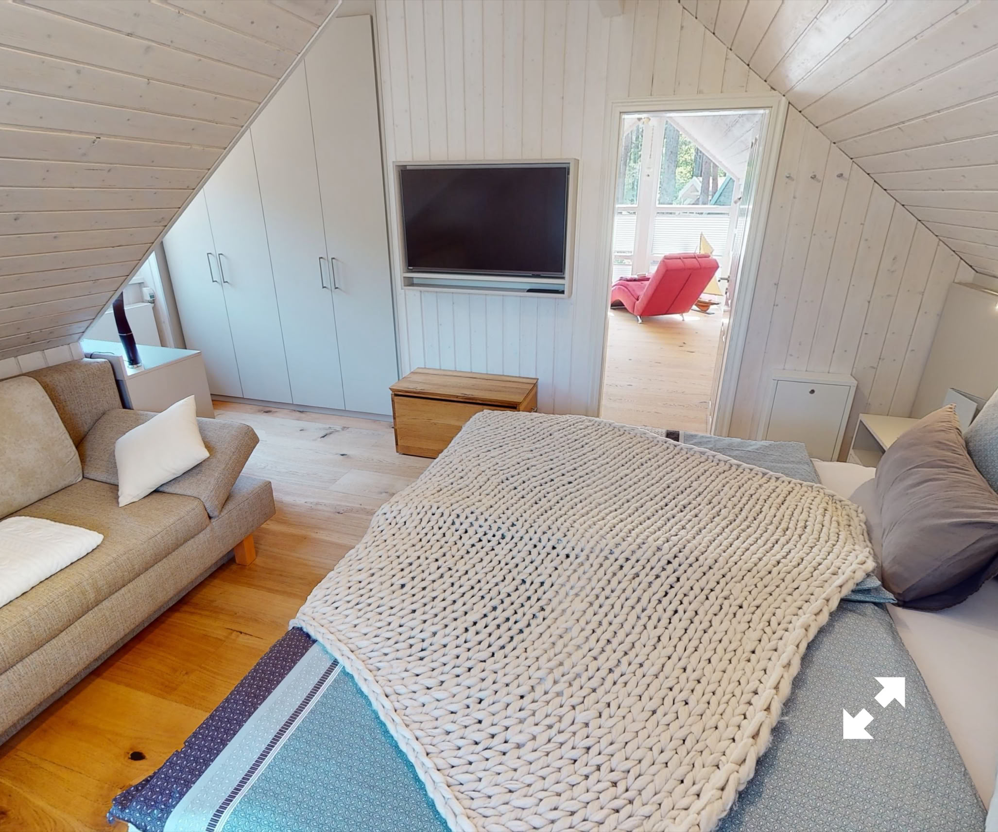 Dachzimmer mit einem Bett, einem Sofa, einem Fernseher an der Wand und einem kleinen Holztisch.