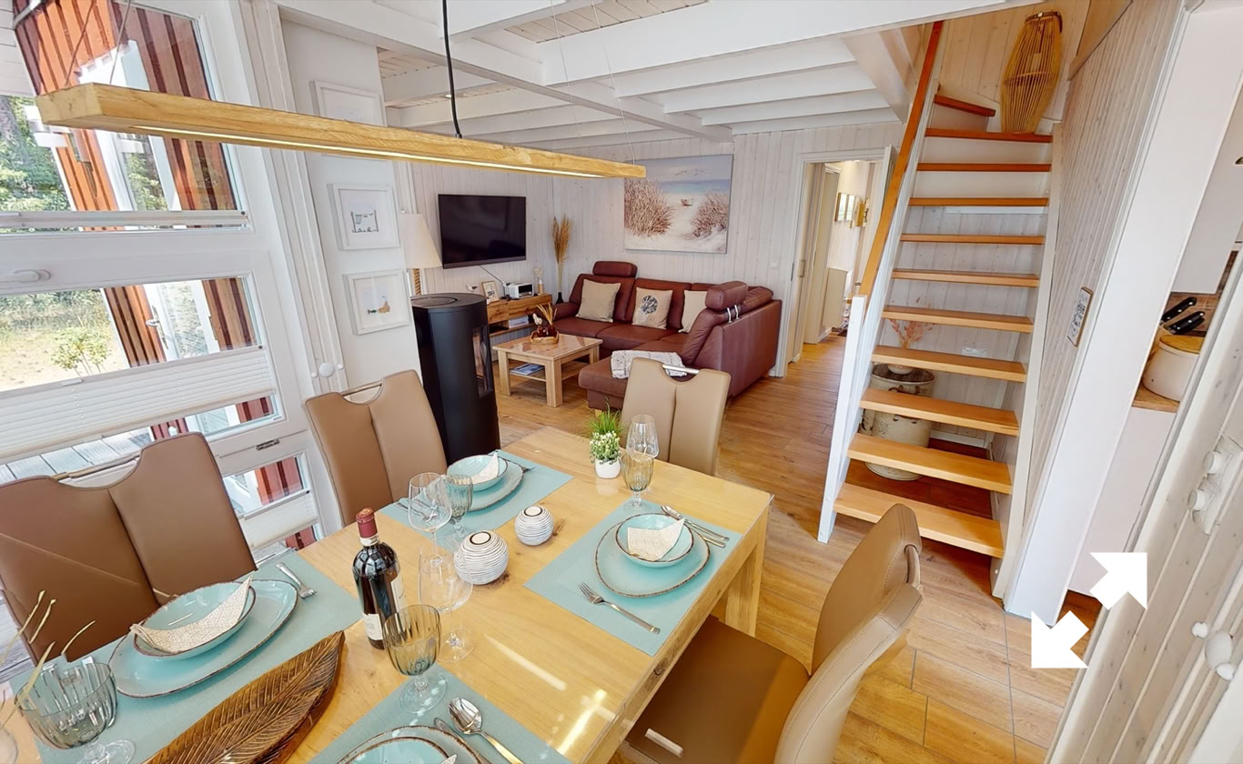 Esszimmer mit gedecktem Tisch, vier Stühlen, Holzboden, Treppe im Hintergrund, Wohnzimmer mit Sofa und Fernseher.