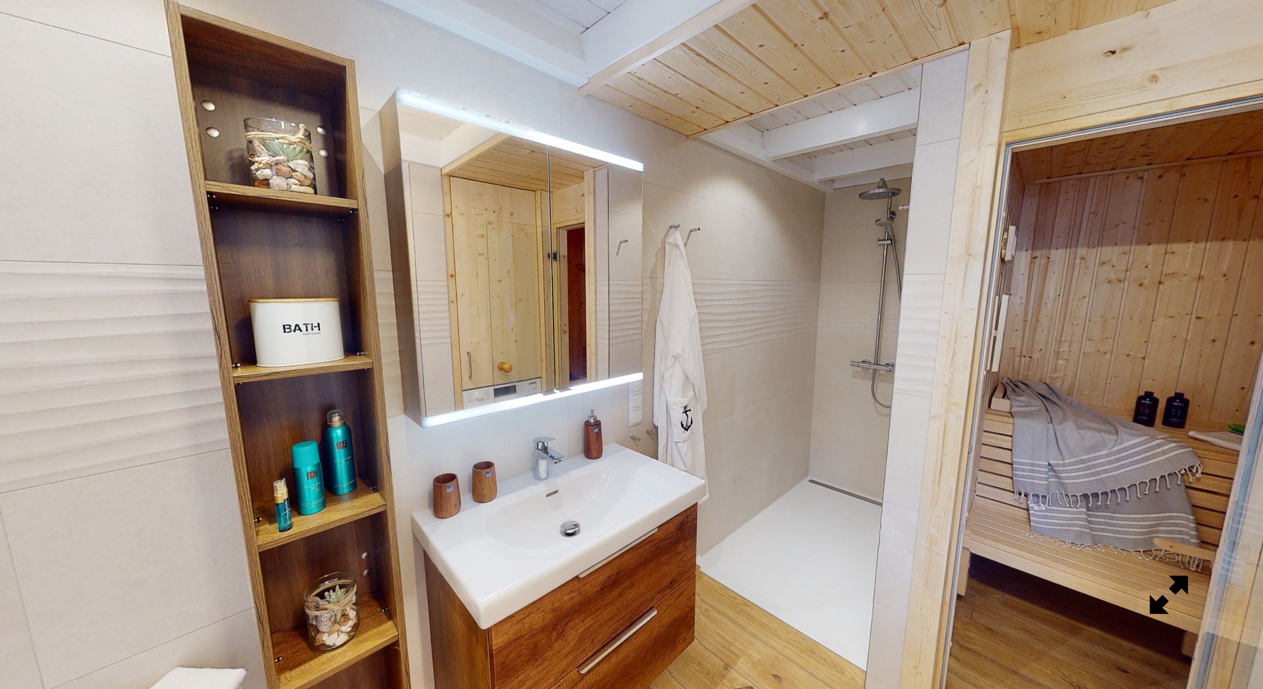 Badezimmer mit Holzdecke, Waschtisch mit Spiegel, Regale mit Pflegeprodukten, Dusche mit weißem Vorhang und angrenzender Sauna.